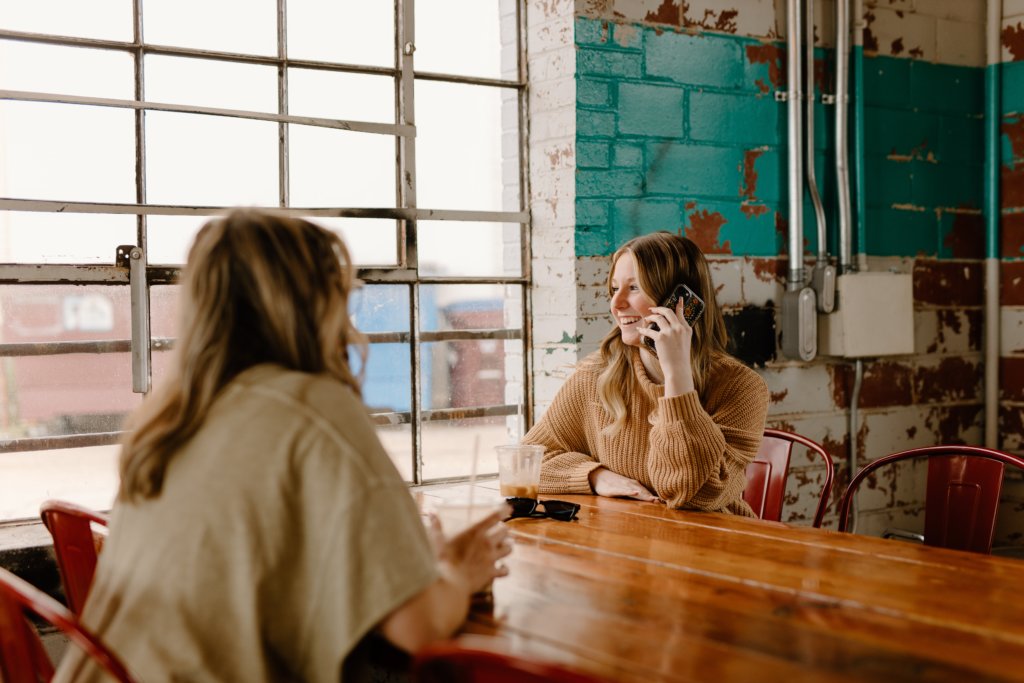 Two girls sitting at table and one is talking on her phone.