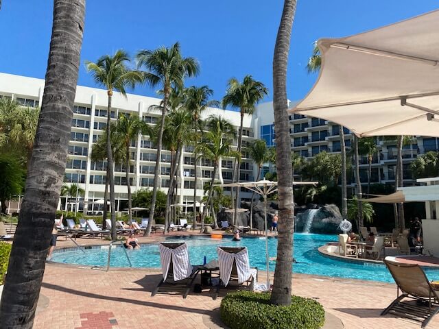 White hotel with green palm trees and pool