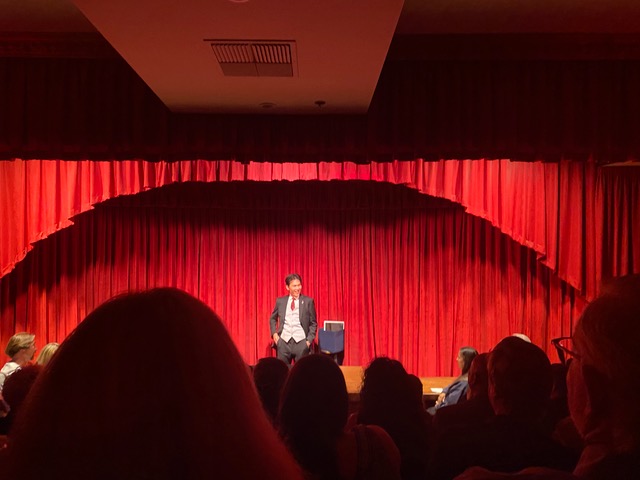 Man in black and white suit in front of red curtain