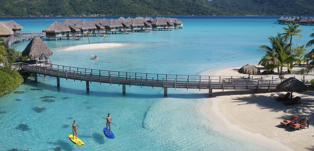 Over the water villas in turquoise water with paddle boarders