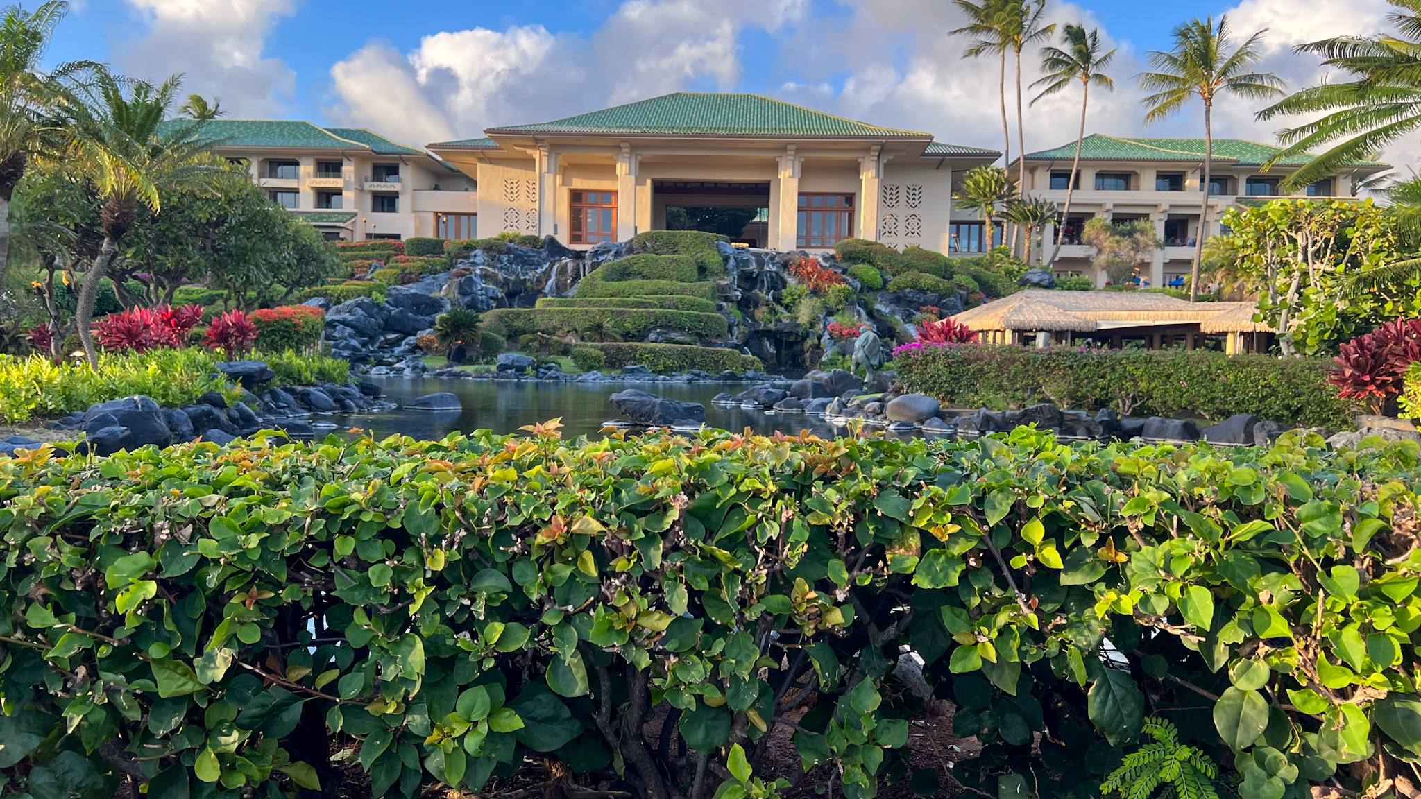 Tan hotel with green roof amongst green foliage