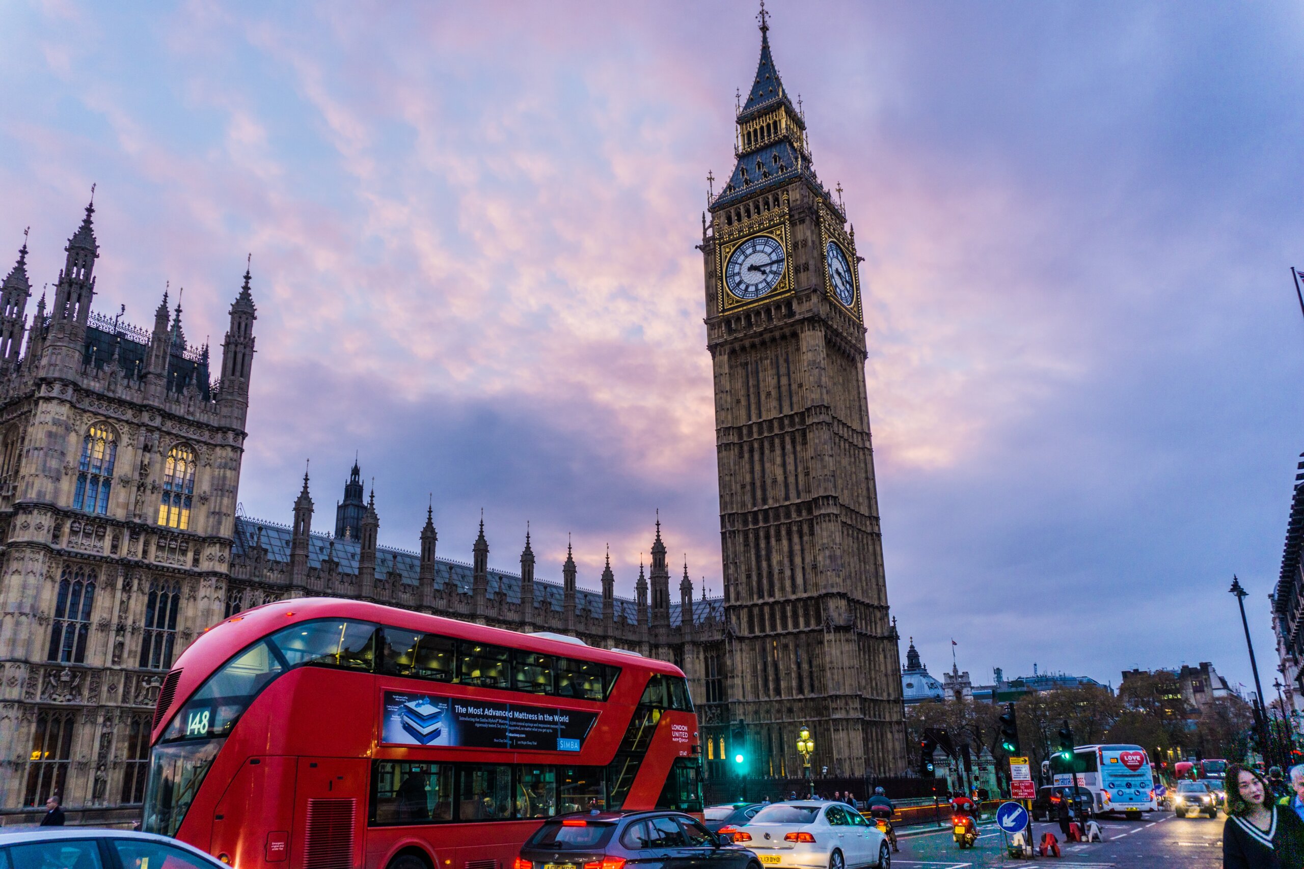 Red double decker bus in front of large tower with clock