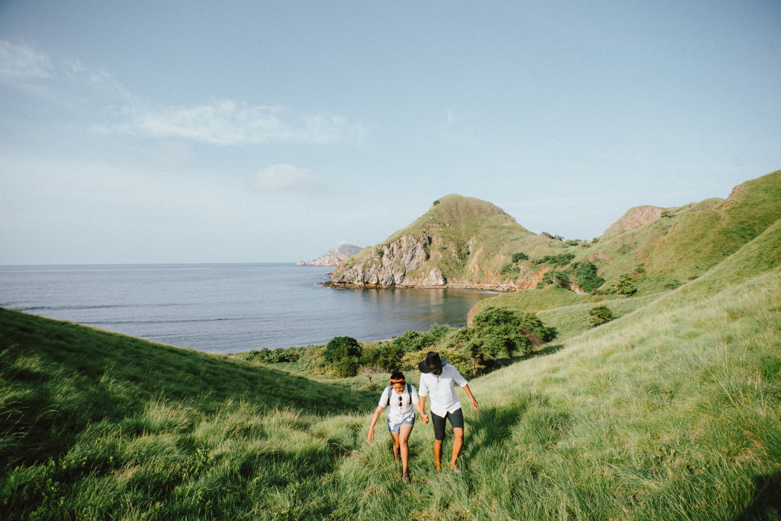 Man and woman walking on green hill with water in background