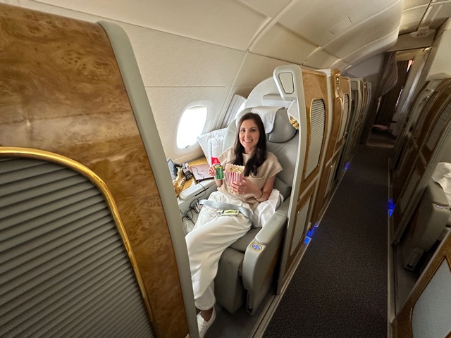 Girl sitting in first class cabin holding popcorn and green can