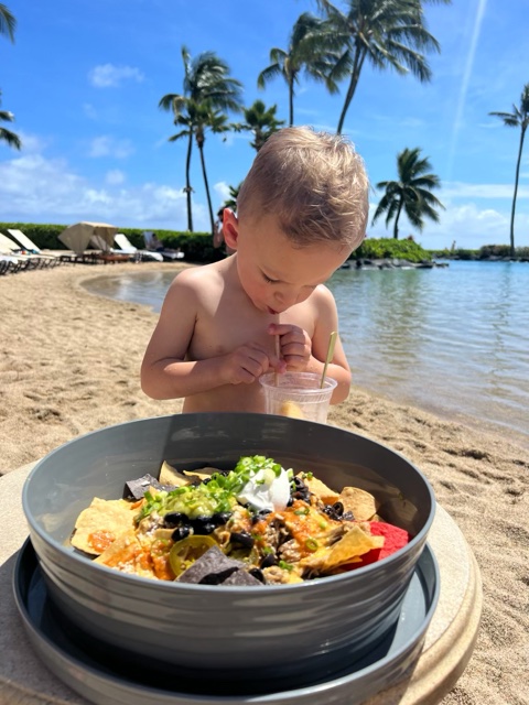 Little boy drinking with straw near lagoon area, nachos in foreground