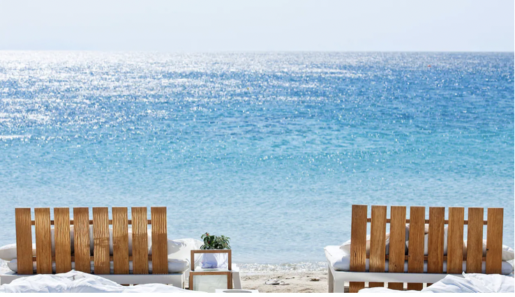 Lounge chairs on beach in front of blue water.