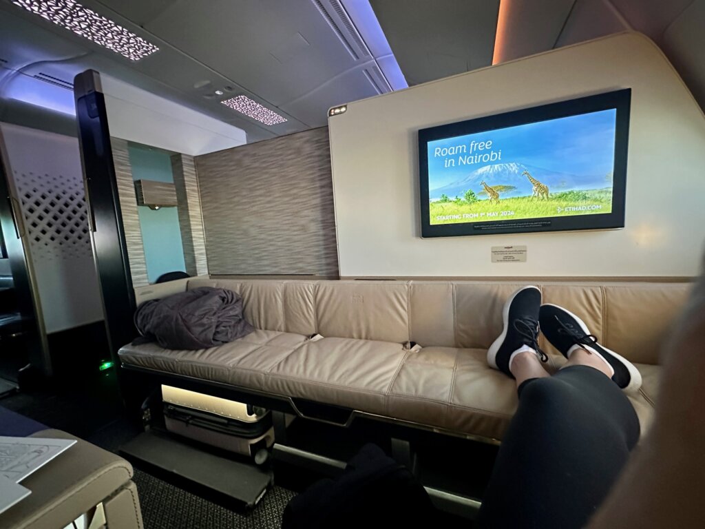 Long bench in airplane with tv above it.