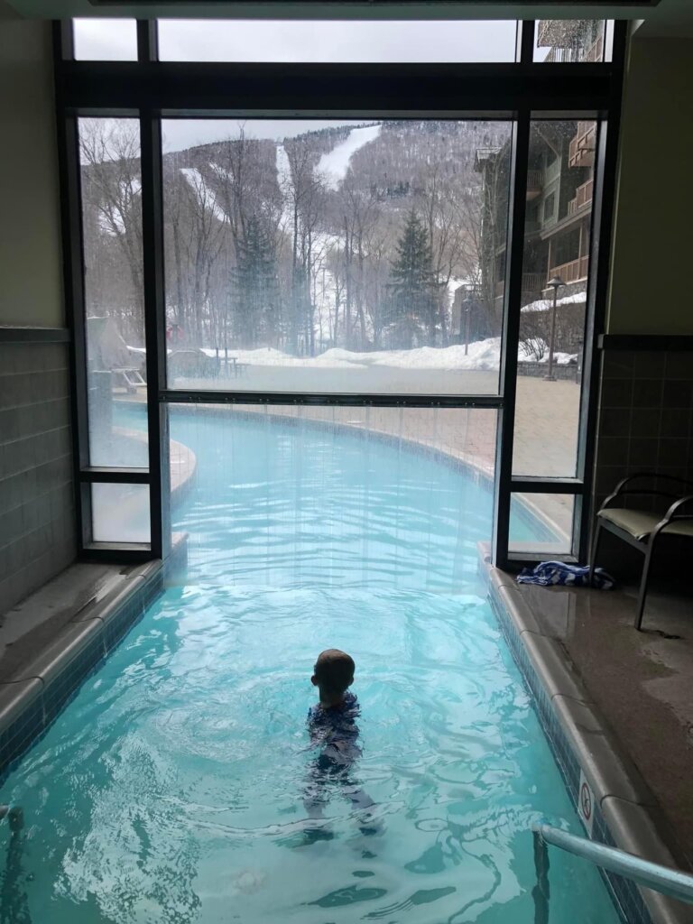 Young child in indoor pool looking at snow outside
