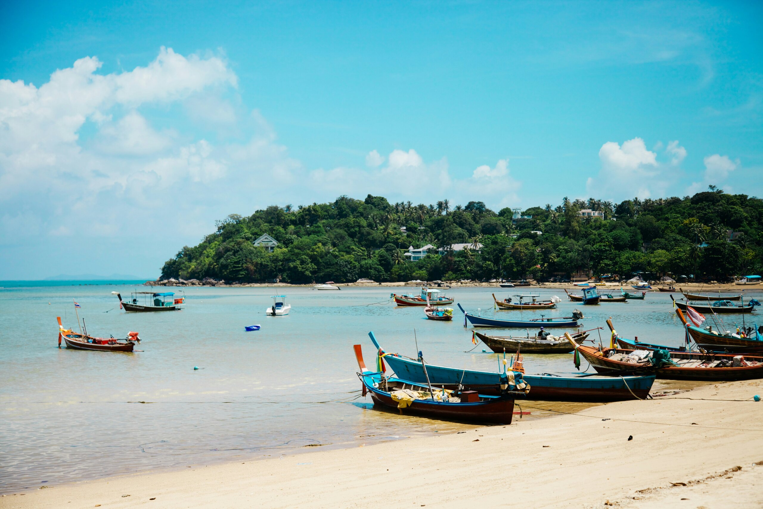 blue water with colorful long tail boats on beach