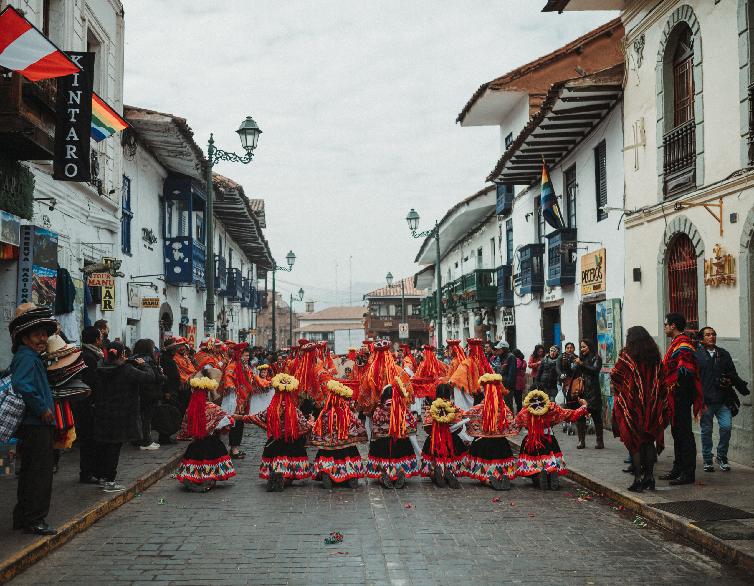 Peruvian dancers dressed in colorful, traditional costume parading down a cobblestone street in Cusco.