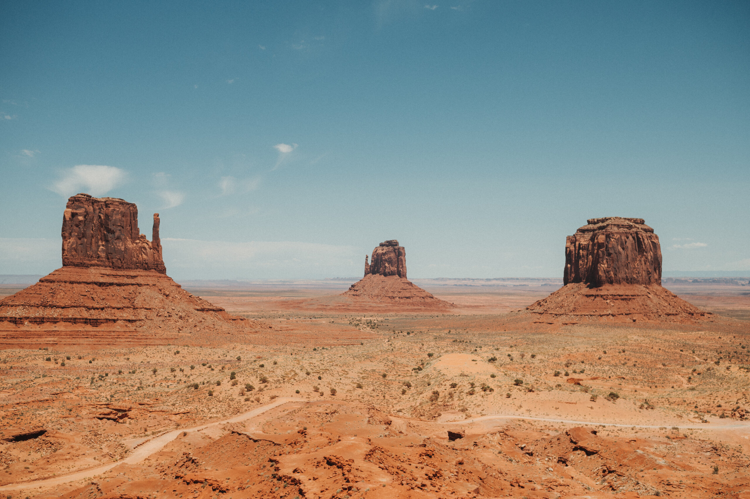 Three rock monuments overlooking Monument Valley against a vibrant blue sky.