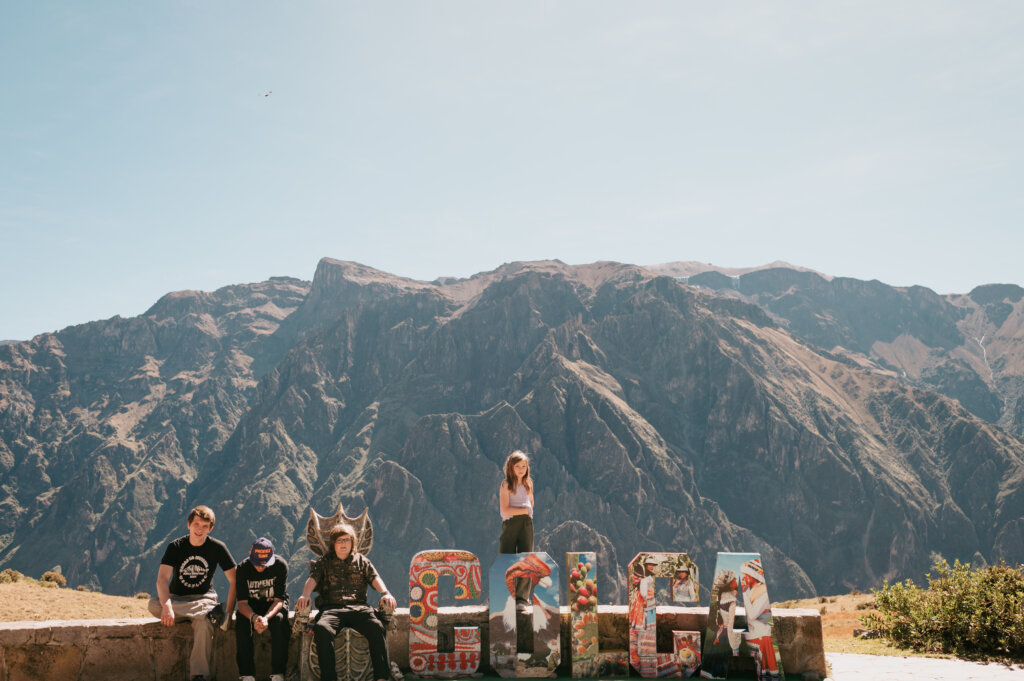Colorful "Colca" sign with children posing on the letters and mountains in the background.