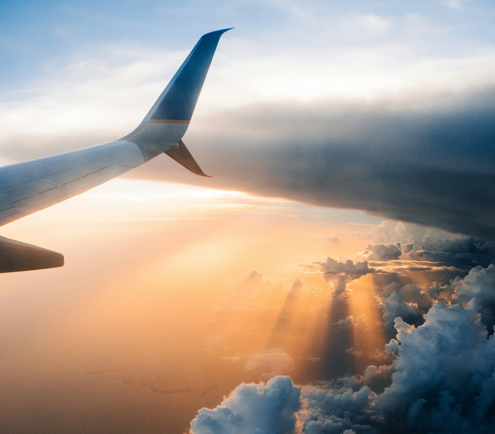 Plane wing over a cloudy sky with the sun setting over water