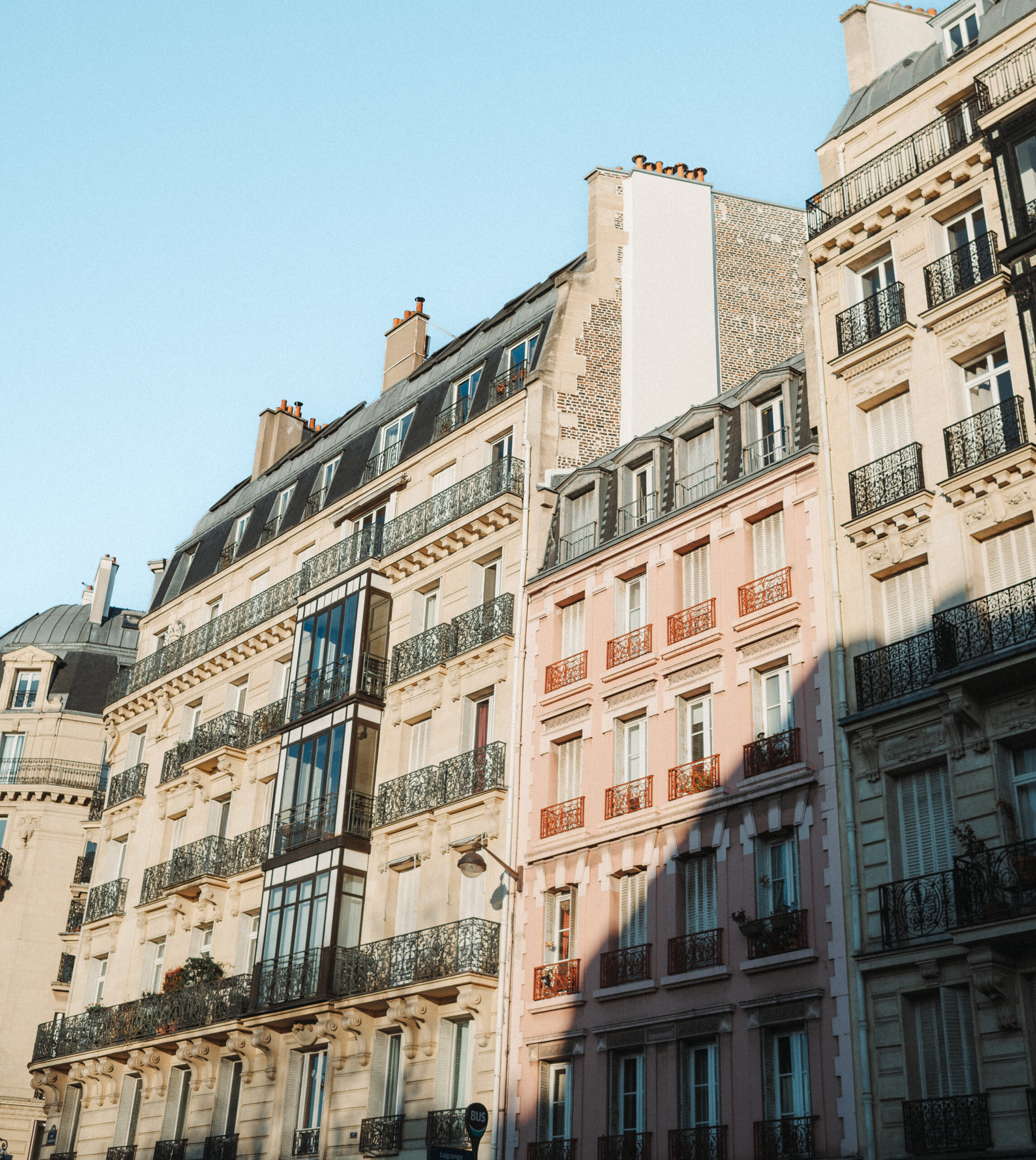 Row of classic Parisian buildings with wrought-iron balconies and mansard roofs.
