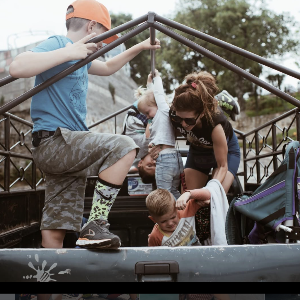 A woman and children standing in the back of a pick-up truck
