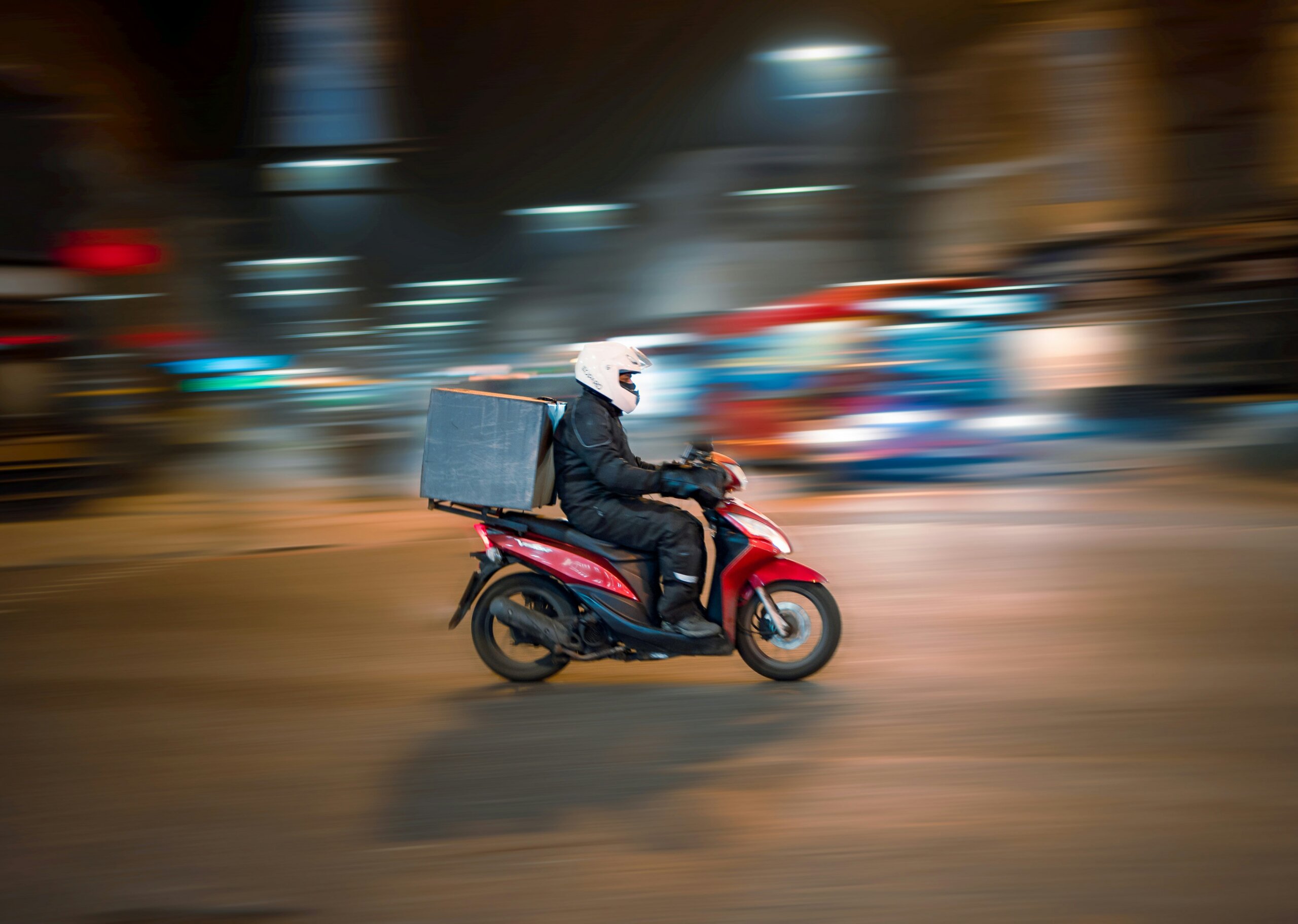 Person riding a motorcycle with a food delivery box on the back, zooming through traffic.