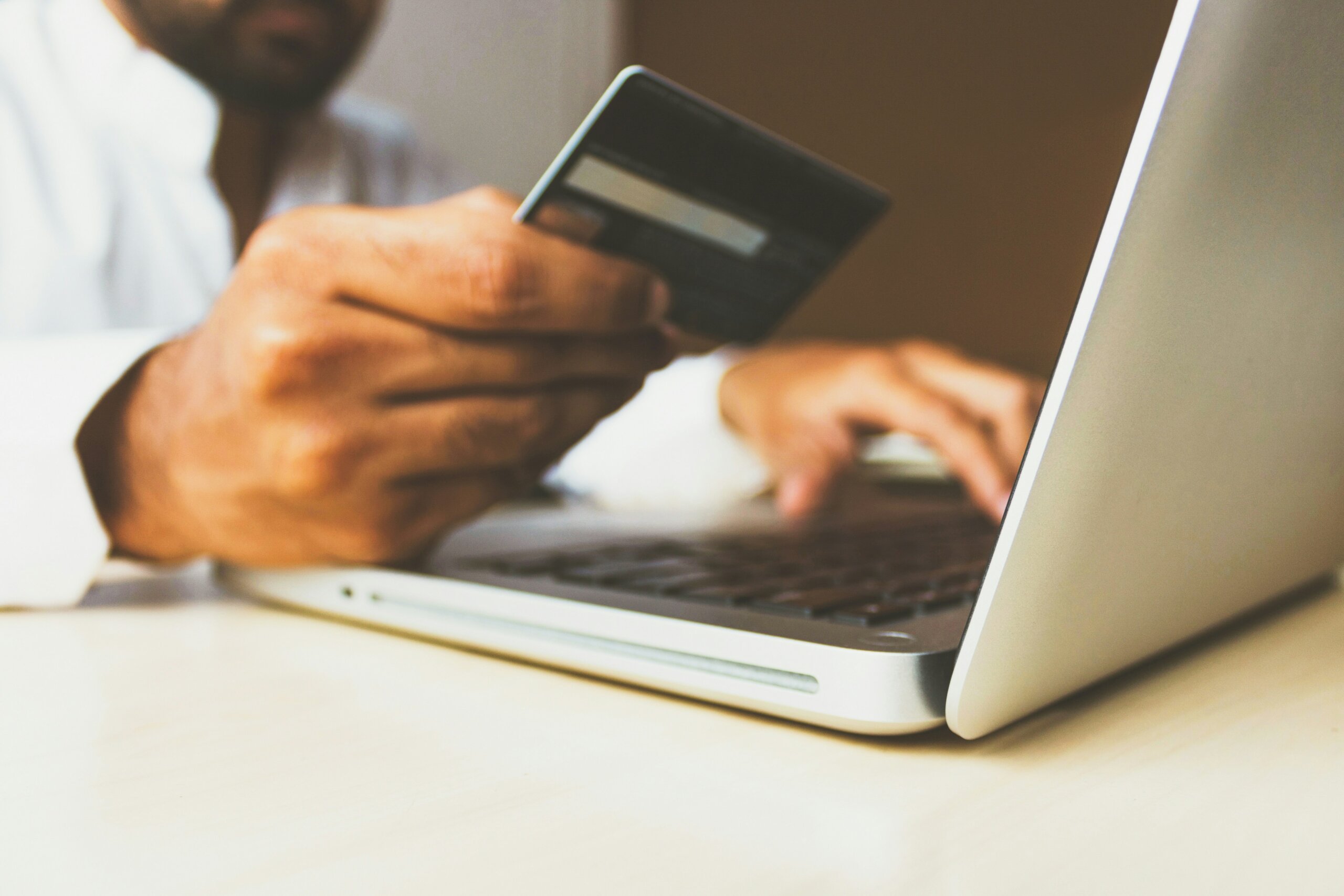 A man sitting at a lap top holding a credit card